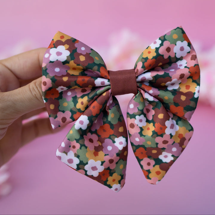 Floral patterned dog sailor bows held against a pink background