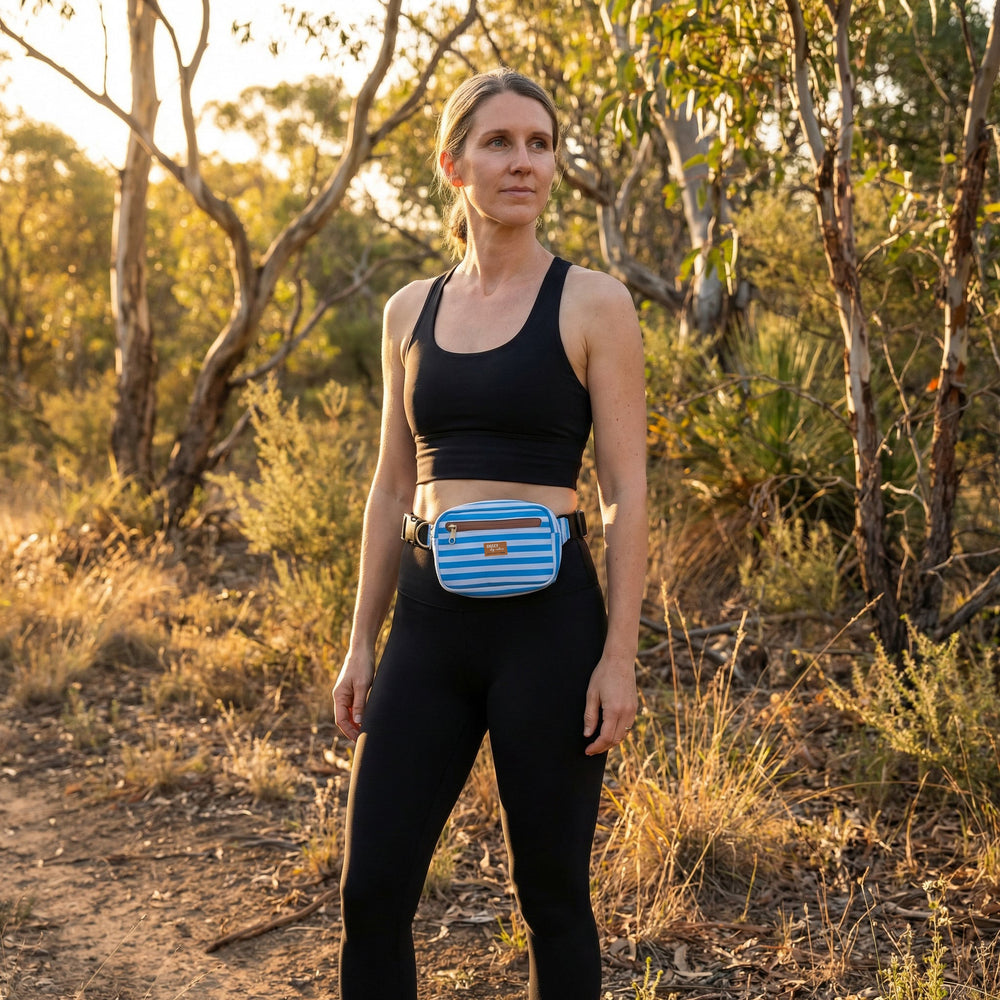 Woman in athletic wear with a blue waist bag standing in a natural setting.