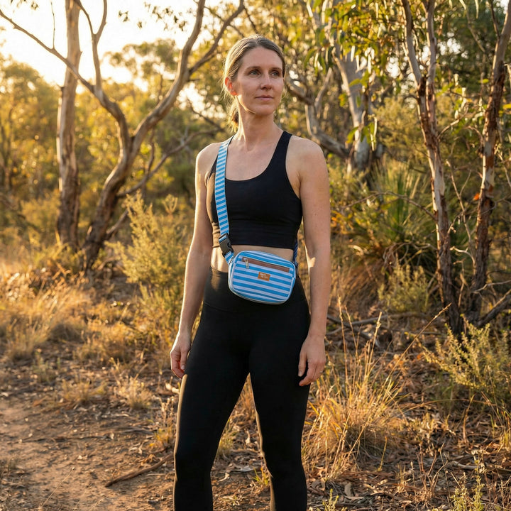 Woman standing in a natural setting with a blue striped bag on her shoulder